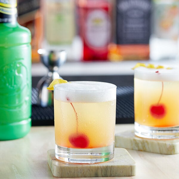 Two glasses of lemon cocktails with a cherry on top and a lemon wedge.