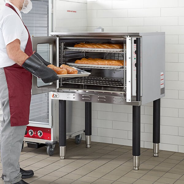 A man wearing a red coat holding a tray of bread in a Cooking Performance Group electric convection oven.