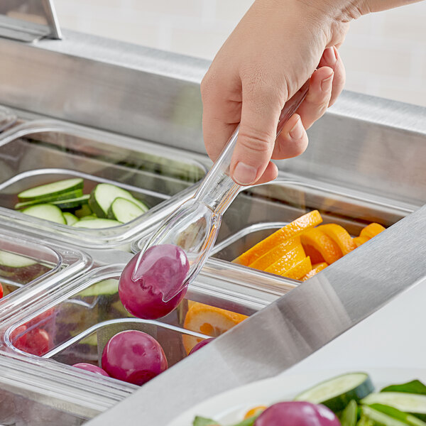 A hand using Carlisle clear salad tongs to serve salad from a salad bar.