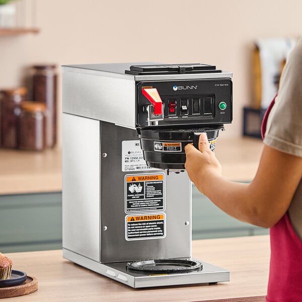 A person using a Bunn commercial coffee machine on a counter.