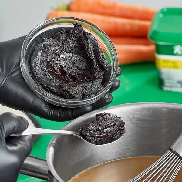 A pair of black gloved hands holding a bowl of Knorr beef base with a whisk.