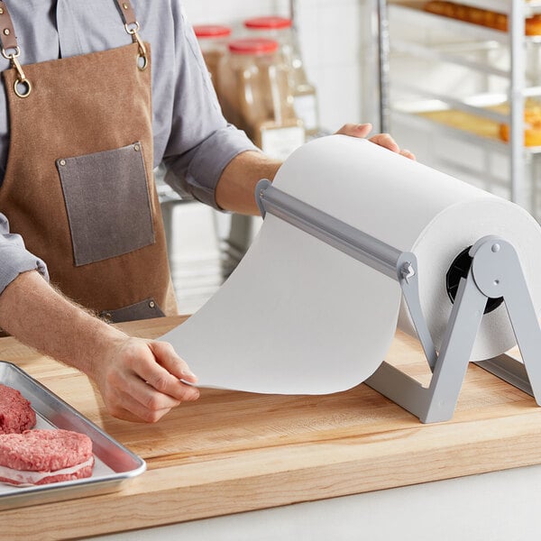 A person in a brown apron using a Choice White Economy Freezer Paper roll to wrap meat.