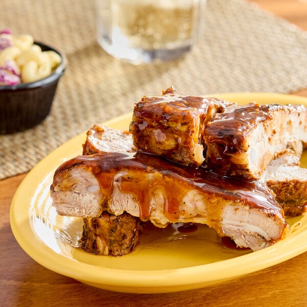 A plate of barbecued ribs covered in a glossy sauce, with a side of macaroni salad in the background.