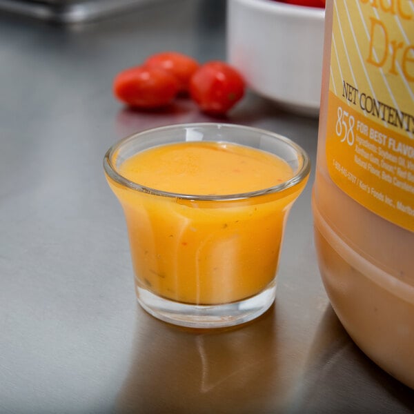 A small glass of orange liquid next to a container of Ken's Foods Golden Italian Dressing.