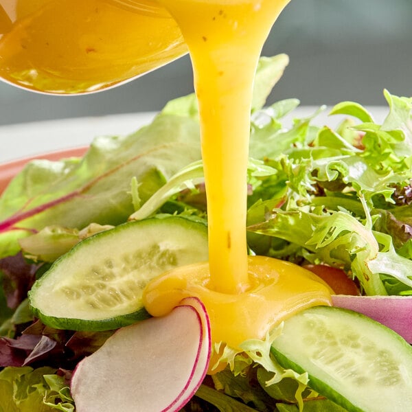A fresh salad with sliced cucumbers and radishes being topped with golden Italian dressing.