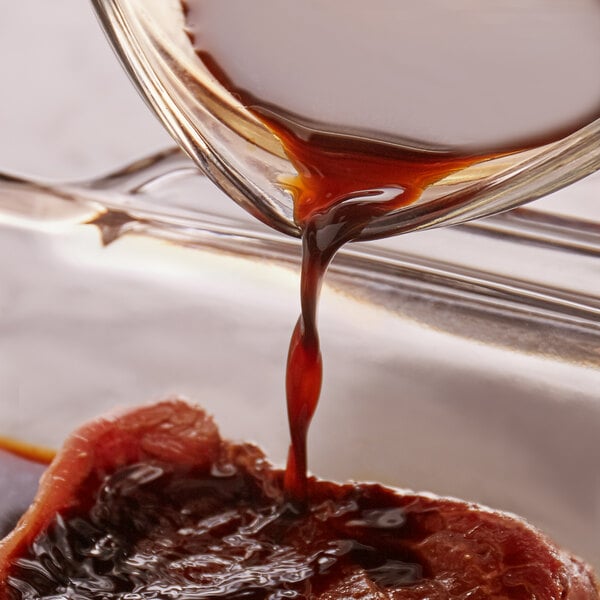 A close-up of Worcestershire sauce being poured from a glass container onto a piece of raw meat.