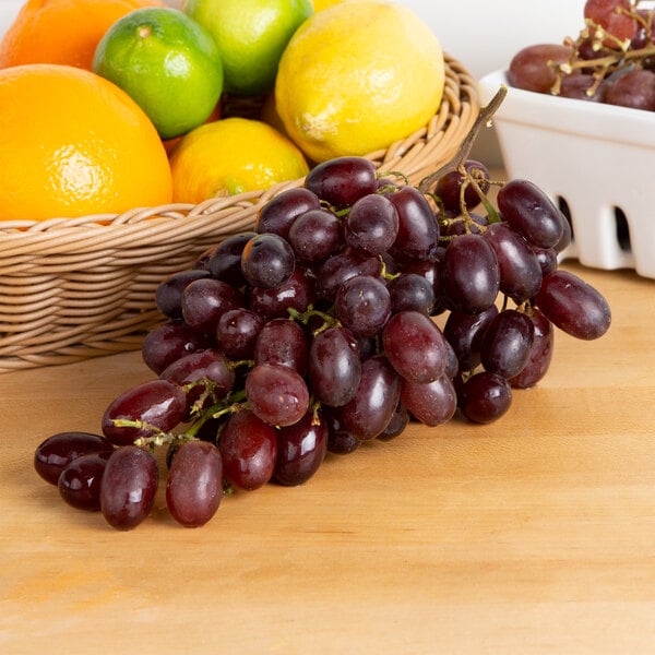 A basket of fruit with oranges and seedless red grapes on a table.