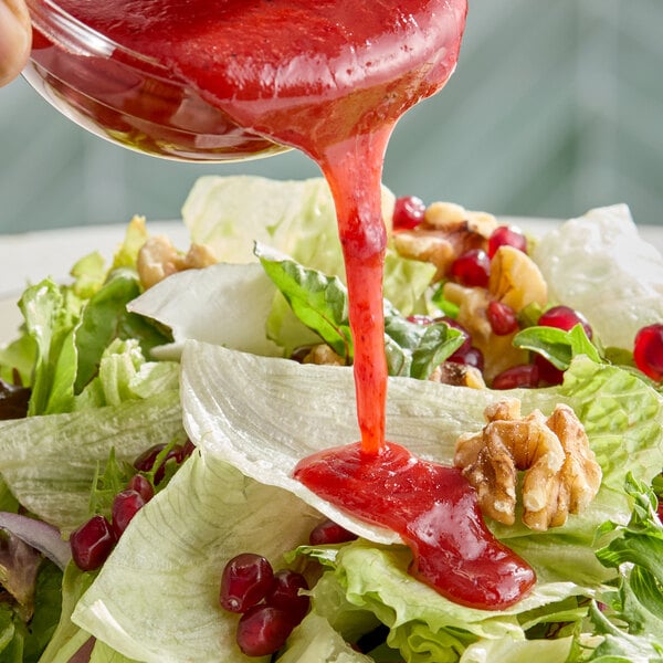A salad with lettuce, walnuts, pomegranate seeds, and a red raspberry vinaigrette dressing being poured on top.