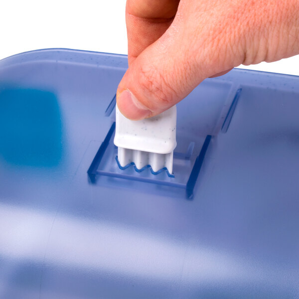 A hand holding a San Jamar Arctic Blue toilet paper dispenser.