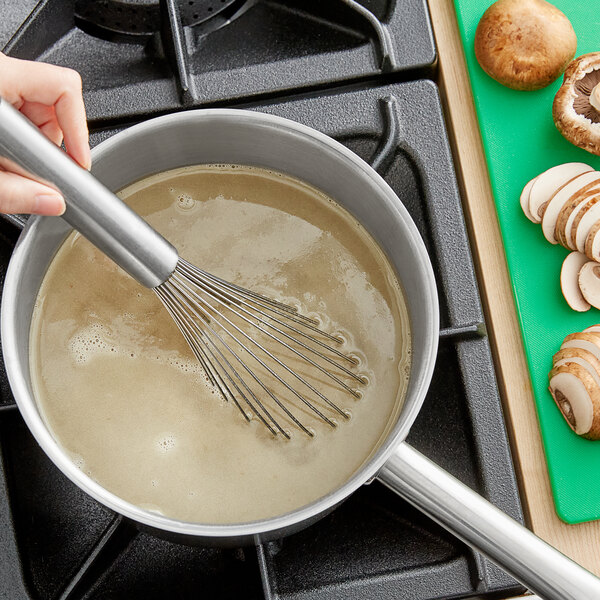 A person stirring brown liquid in a pot with a metal whisk.