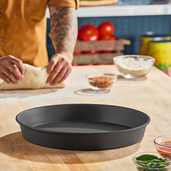 A round, hard coat anodized aluminum pizza pan with tapered sides, measuring 14 inches in diameter and 2 inches deep.