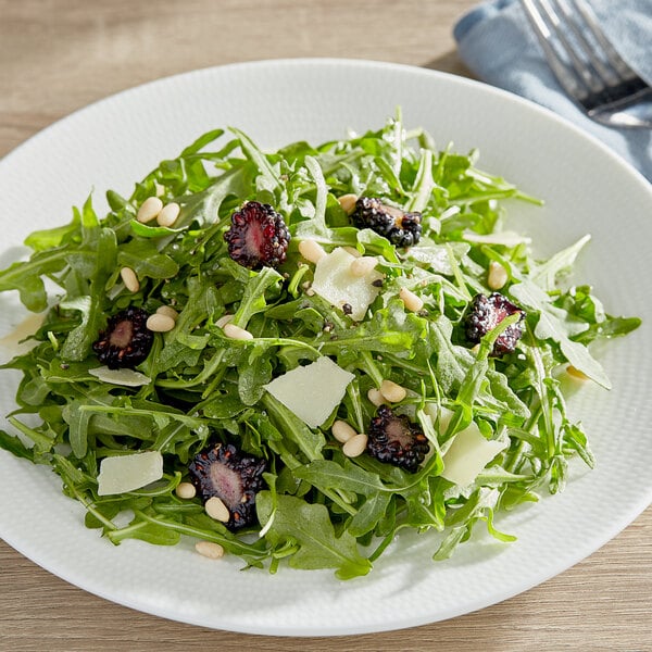 A plate of salad with arugula, blackberries, and pine nuts.