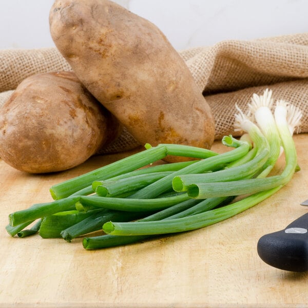 A cutting board with a bunch of green onions and potatoes on it.