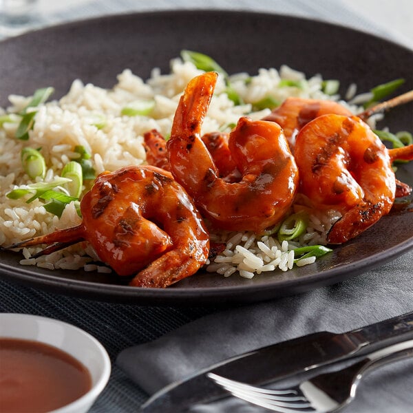 A plate of grilled shrimp skewers coated in a spicy sauce, served over white rice with sliced green onions.