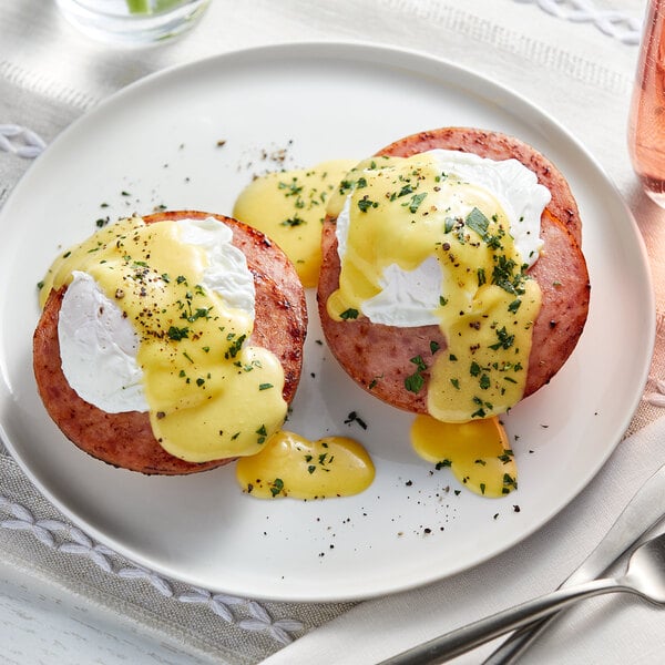 A white plate with eggs benedict and yellow and white sauce.