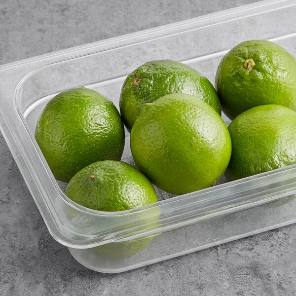 A plastic container of fresh limes on a counter.