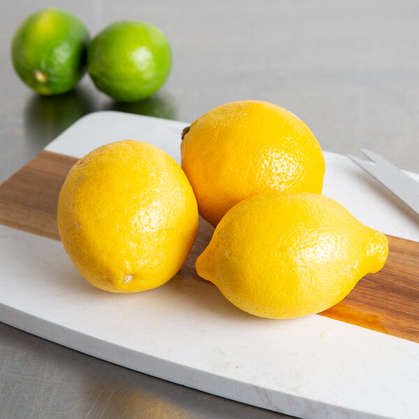 A cutting board with three Choice lemons and a knife on a table.
