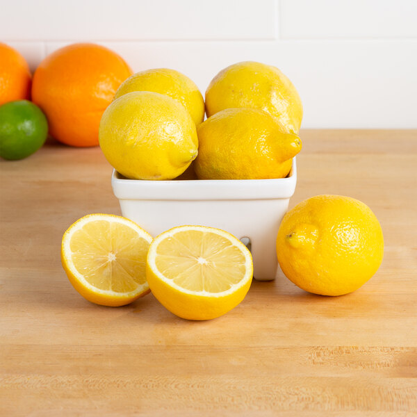 A bowl of lemons on a table with a lemon cut in half.