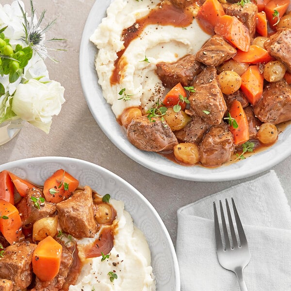 A bowl of beef stew with meat, carrots, and potatoes.