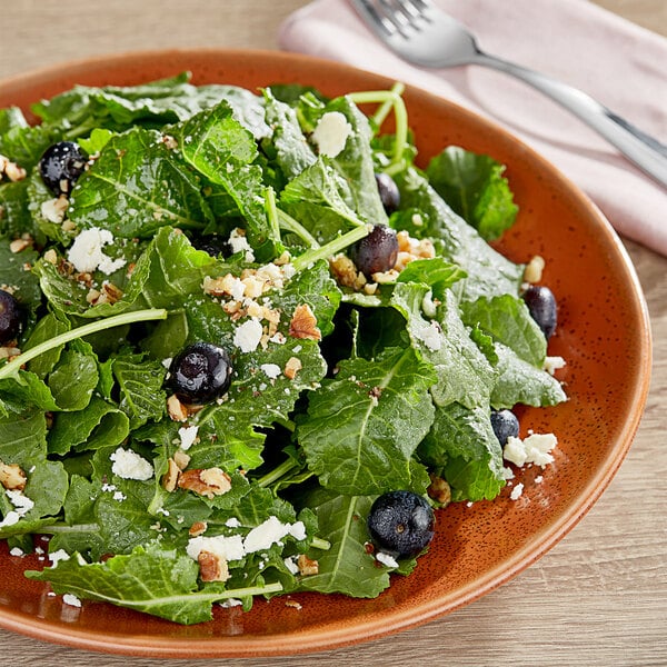 A plate of baby green kale salad with blueberries and nuts.