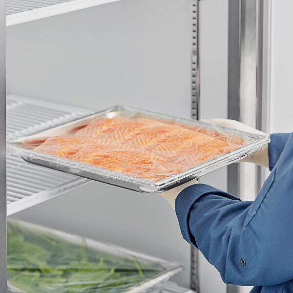 A person holding a Vollrath stainless steel steam table pan filled with food.