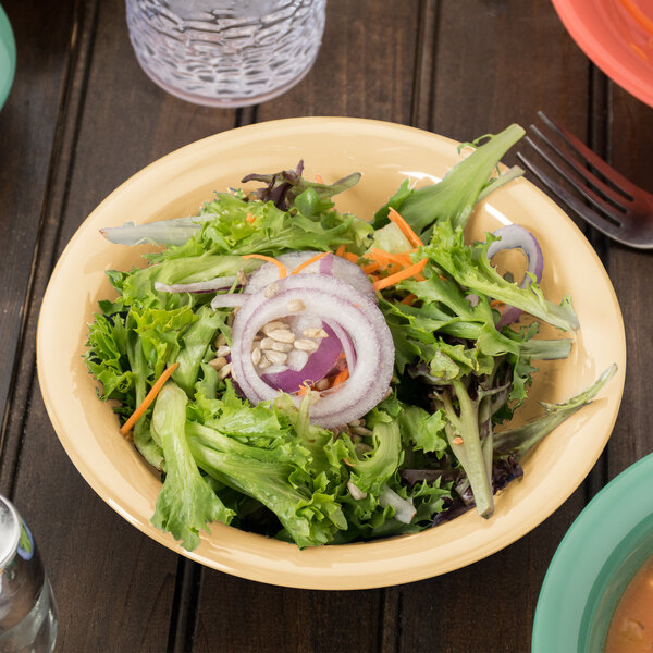 A bowl of squash salad with carrots and onions in a yellow Diamond Harvest melamine bowl on a table.