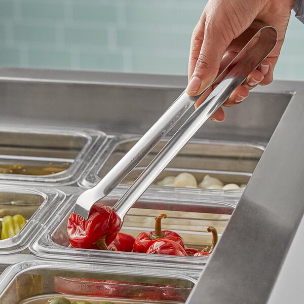 A person using Vollrath Pom Tongs to serve food from a tray.