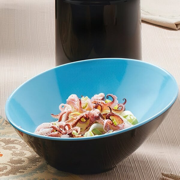 A black and blue slanted melamine bowl with food inside on a table.