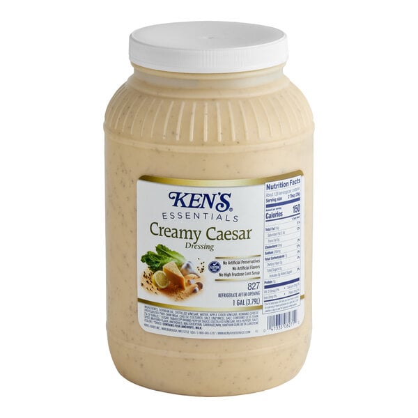 A 1-gallon plastic jar of Ken's Essentials Creamy Caesar Dressing.