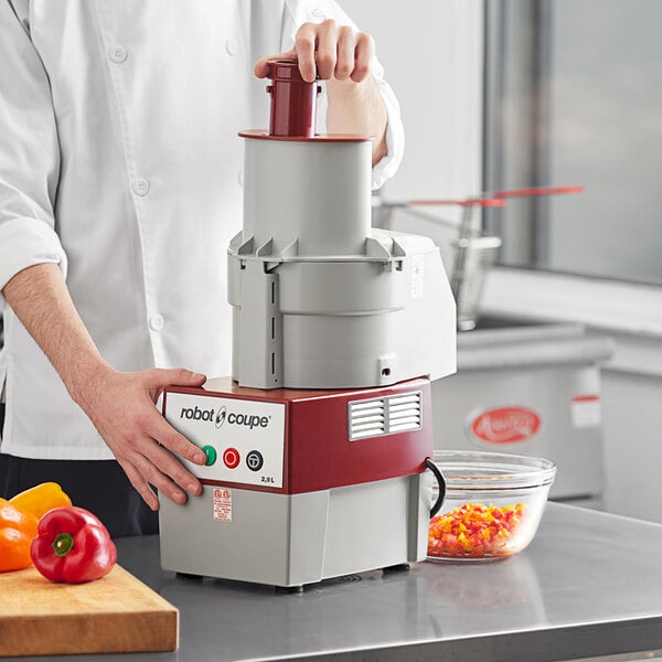A man using a Robot Coupe commercial food processor to dice food in a clear bowl.