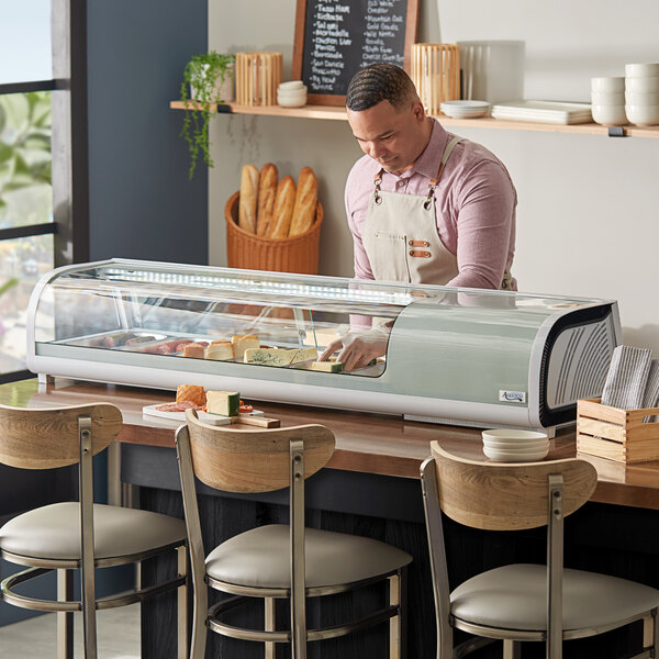 A man standing behind a counter with food in a glass case.