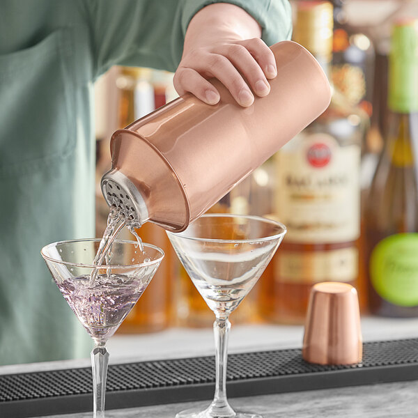 A bartender pouring a drink from an Acopa copper cocktail shaker into a martini glass.