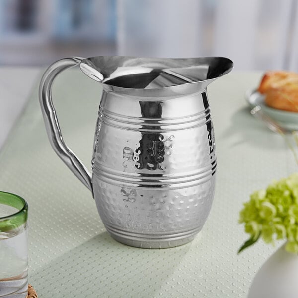 An Acopa stainless steel bell pitcher on a table.