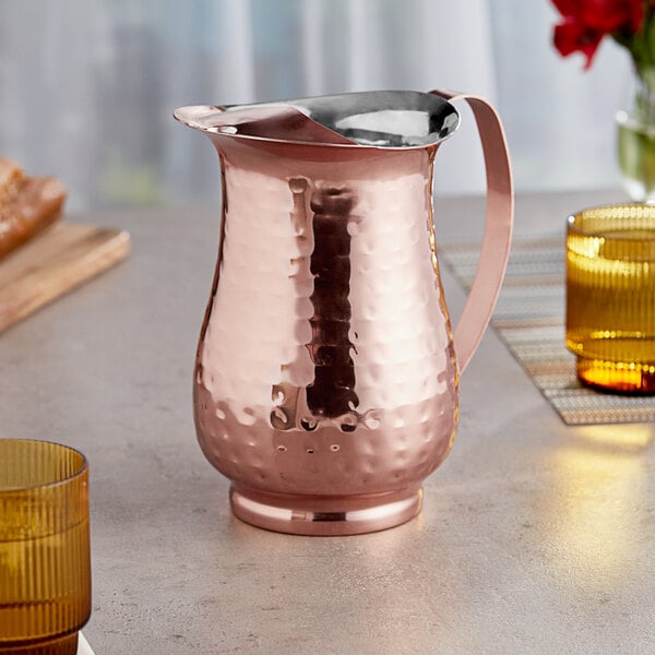 An Acopa copper pitcher with a metal handle on a table.