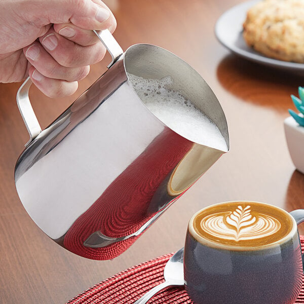 Barista pouring milk from a frothing pitcher to make latte art