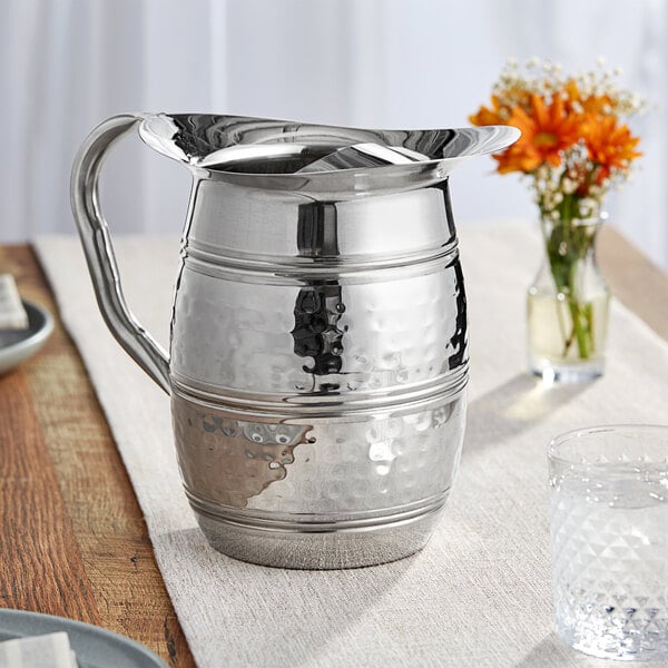 An Acopa stainless steel bell pitcher on a table with flowers.