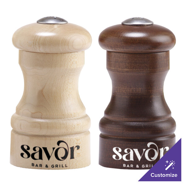 Two Chef Specialties customizable walnut pepper shakers on a table with a wooden salt shaker.