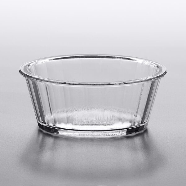 A clear plastic fluted ramekin on a gray surface.