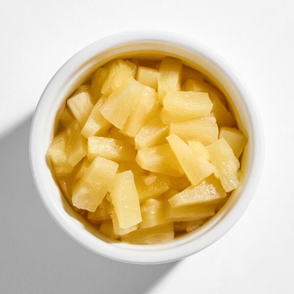 A white bowl filled with yellow pineapple tidbits in juice, viewed from above.