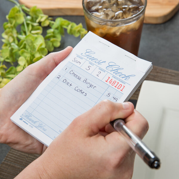 A person holding an Adams Guest Check book and pen.