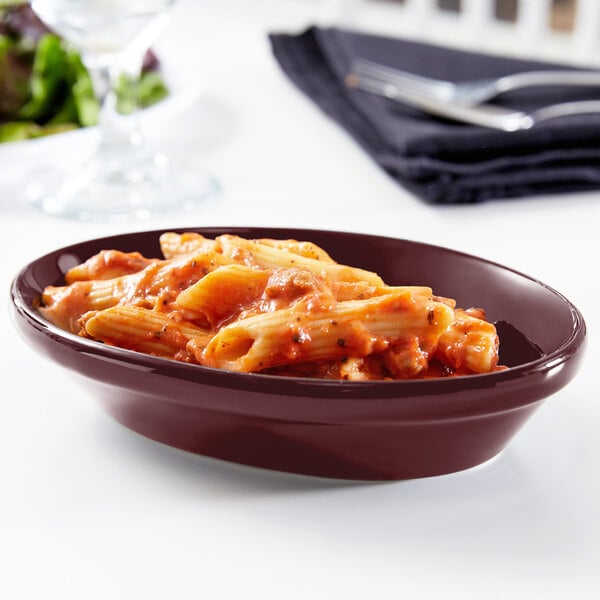 A Tuxton burgundy oval china nesting baker filled with pasta and sauce on a table.