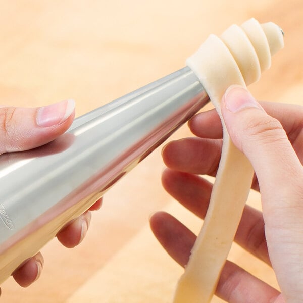 A person using an Ateco stainless steel cream horn mold for pastry.