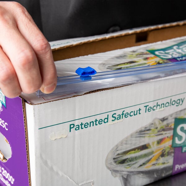 A hand using a Choice 24" Replacement Safety Slide Cutter to open a zip lock bag on a box.