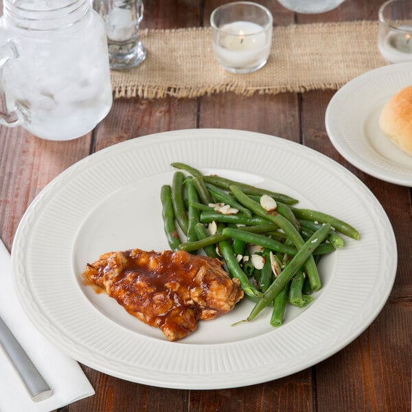 An ivory china plate with green beans and chicken on it.