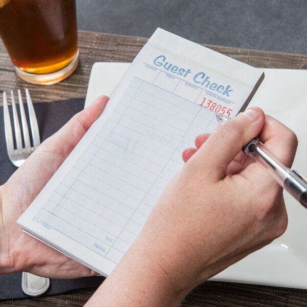 A person holding a Tops carbonless guest check book with a pen.