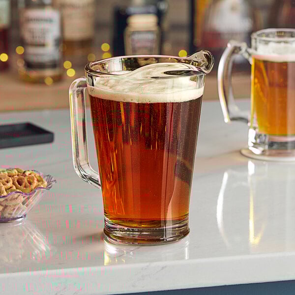 A Libbey pitcher of beer on a counter with a glass of beer.