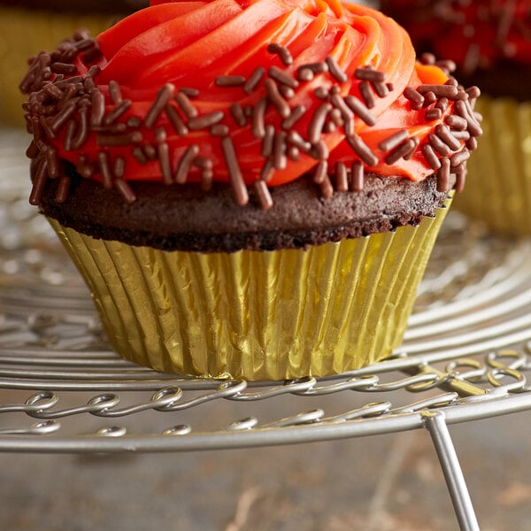 A cupcake with orange frosting and sprinkles in a gold Ateco baking cup.