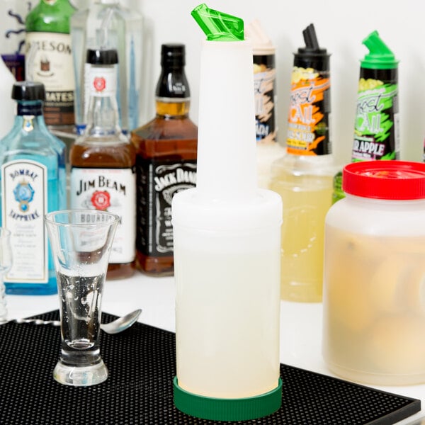 A close-up of a Carlisle white pour container with a green spout and cap on a counter.