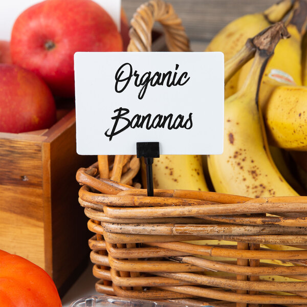 A basket of organic bananas with American Metalcraft Mini White Chalk Cards on a counter.