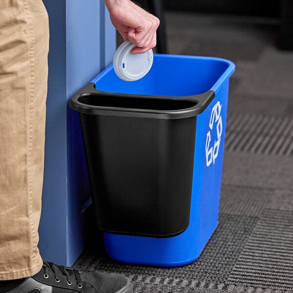 A black Rubbermaid oval wastebasket with a white lid.